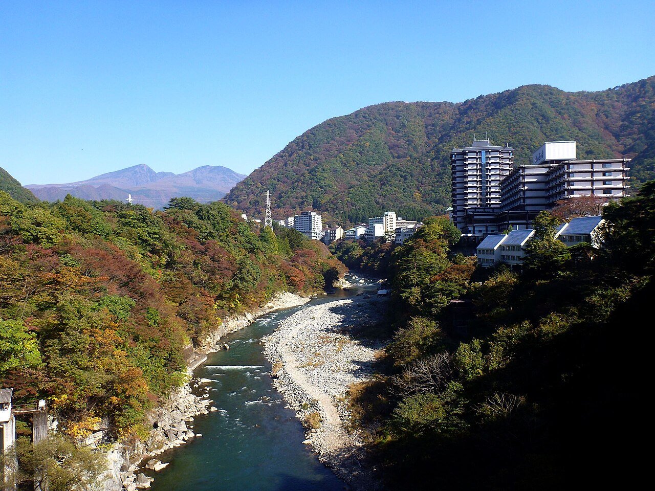 秋の鬼怒川温泉の渓谷と、渓谷沿いに並ぶ温泉街の写真。