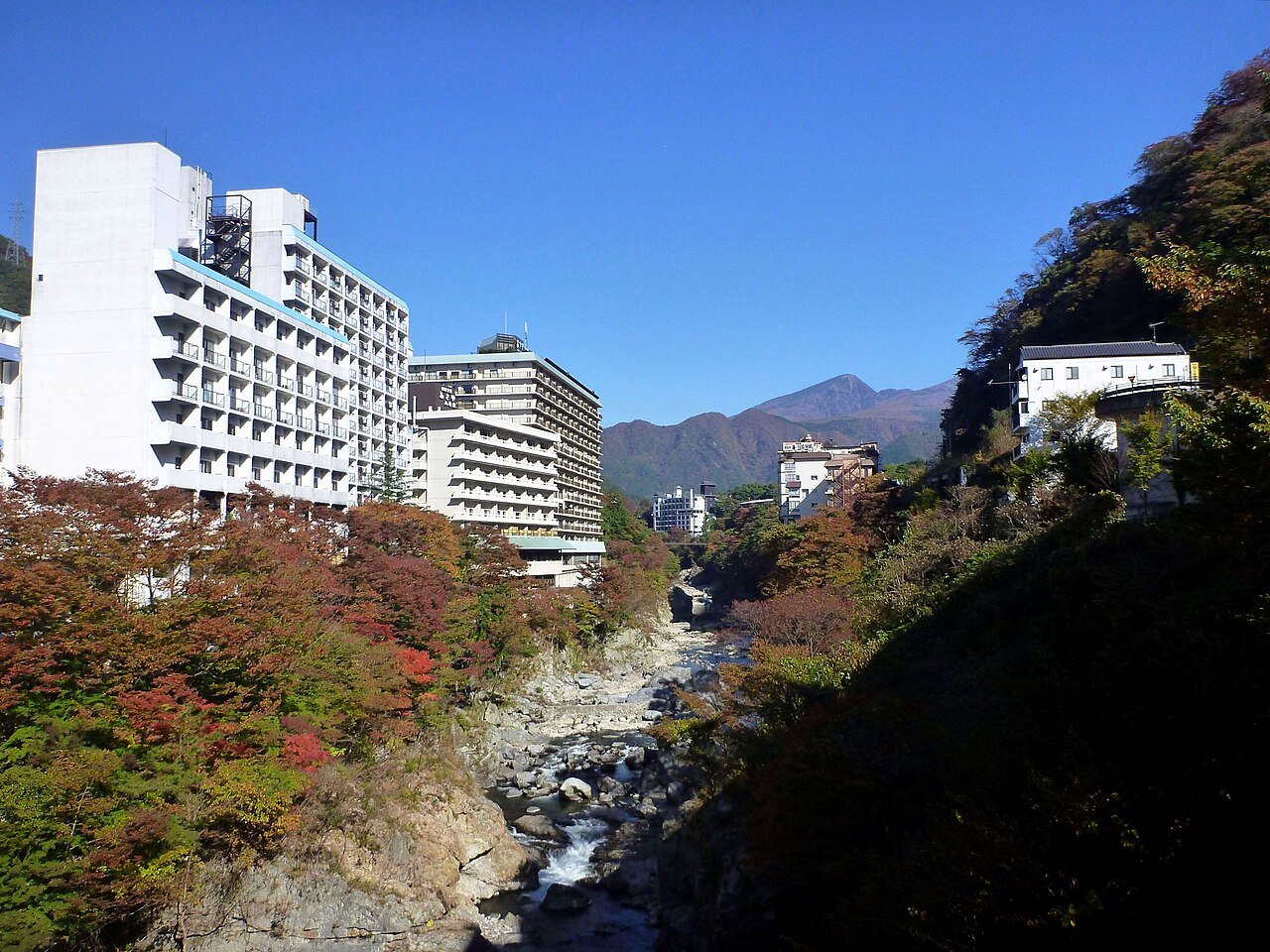 紅葉した渓谷の上に宿やホテルが並ぶ、秋の鬼怒川温泉の写真。