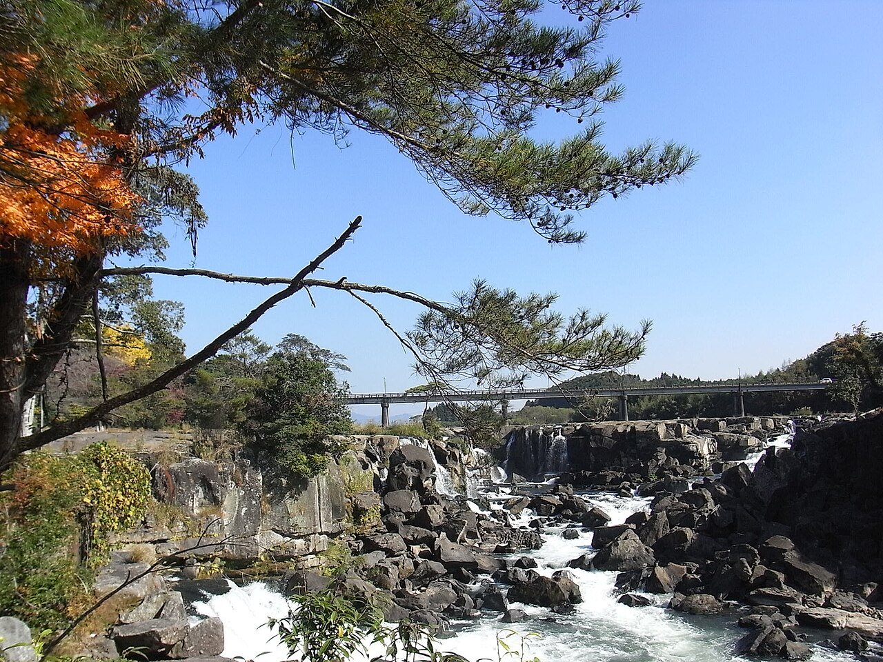 岩の間を流れる曽木の滝と紅葉の写真。